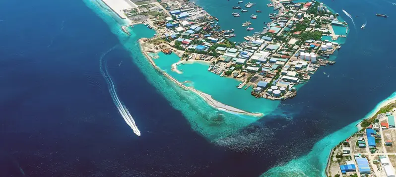 Ett fotografi taget från ett flygplan som visar delar av Maldiverna uppifrån där människor bor i mycket lågt liggande områden och väldigt nära havet. 