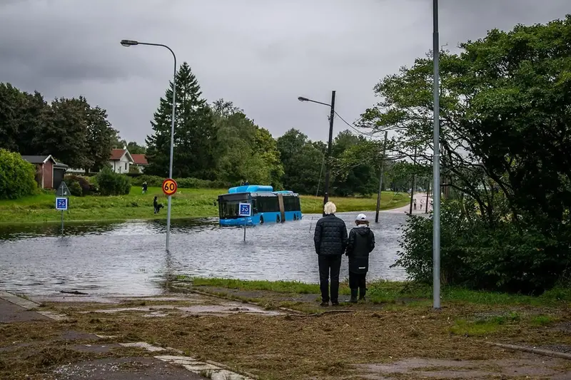 Ett par står intill en översvämmad väg och tittar på en buss som fastnat i vattenmassorna.