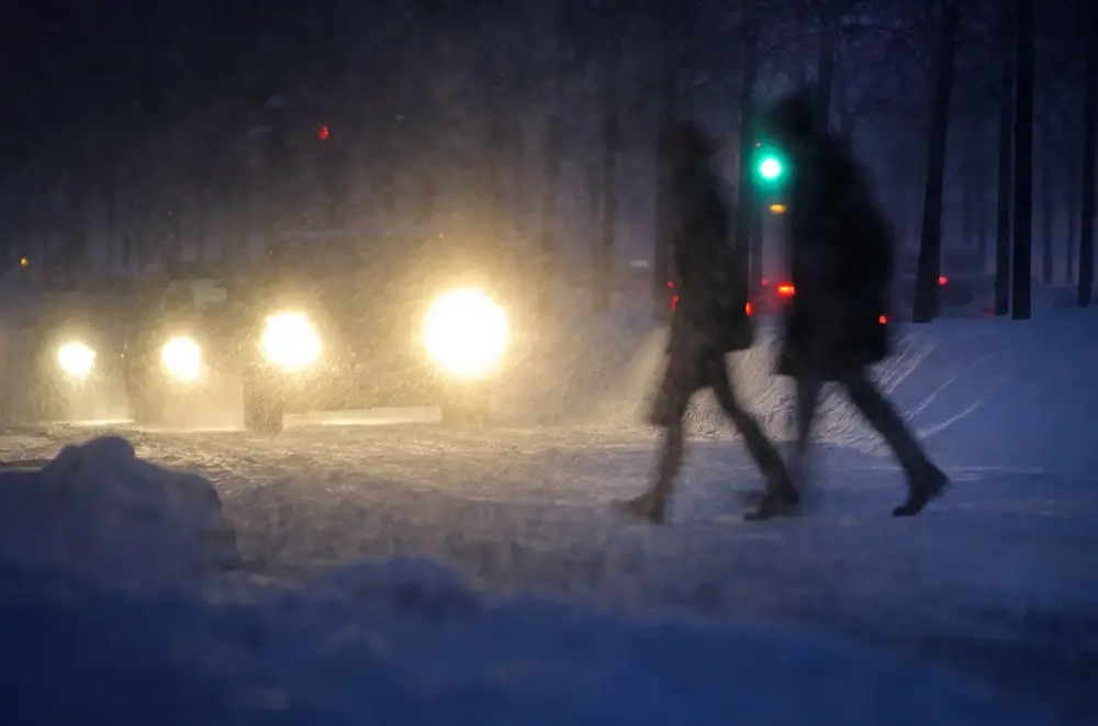 Snöfall i kvällningen med bilar och fotgängare